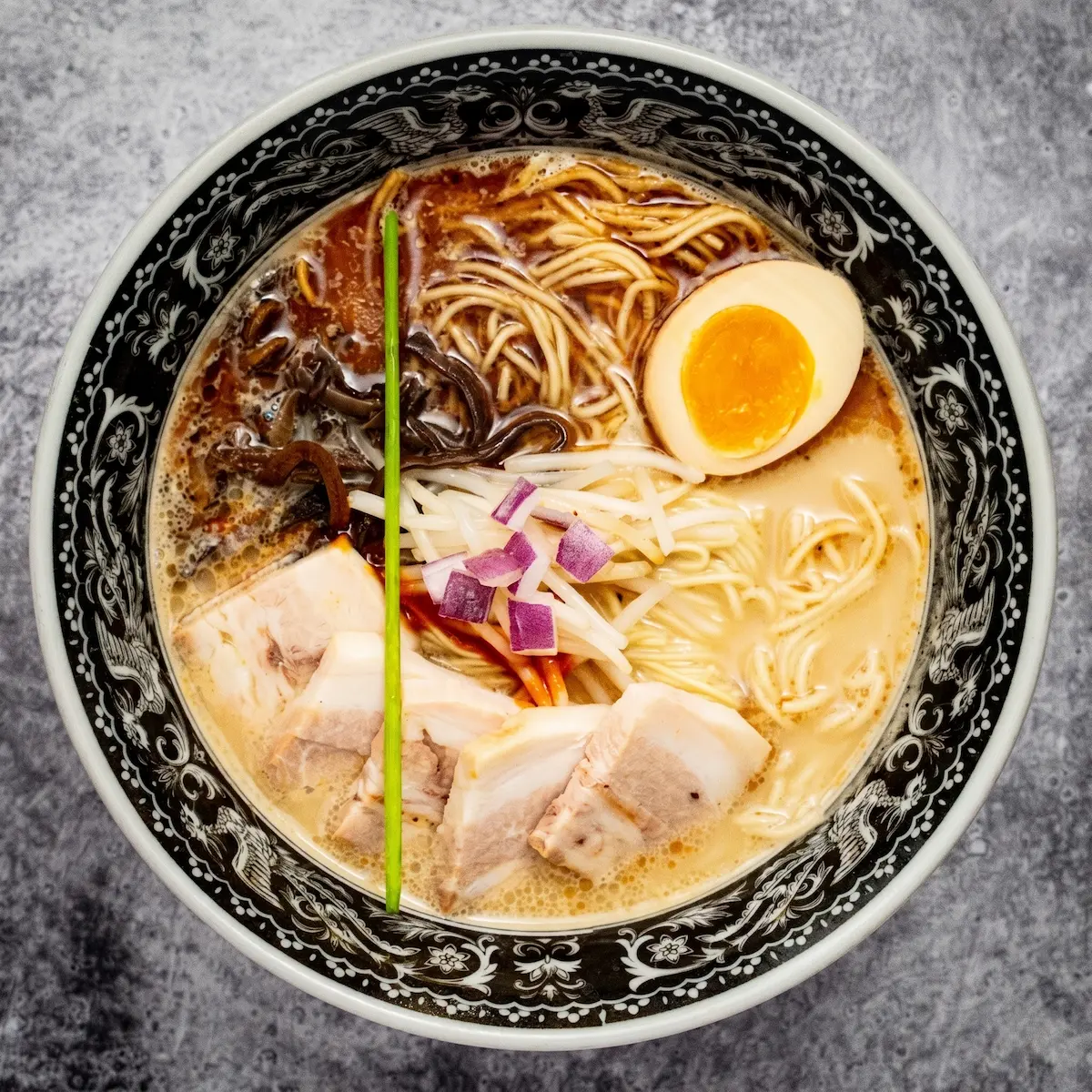 Tonkotsu Black - A bowl of well-balanced pork broth ramen with medium straight noodles, pork chashu, black garlic oil, umami paste, kikurage mushroom, bean sprouts, and a soft-boiled egg